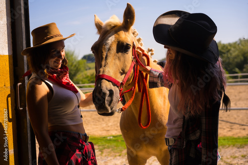 Silhouette of two cowgirl women entering the stable with a horse from a horse, with South American outfits