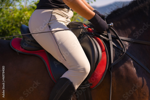 Unrecognizable girl riding on a horse riding with a brown horse, dressed black rider with safety cap © unai