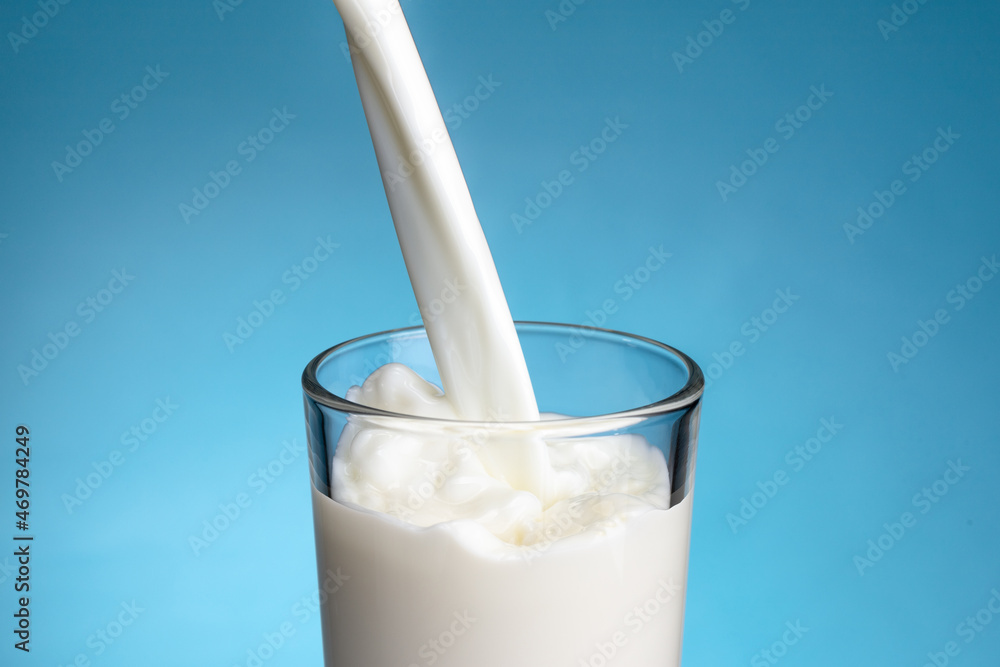 Pouring milk into glass on blue background Pouring milk into glass on blue background