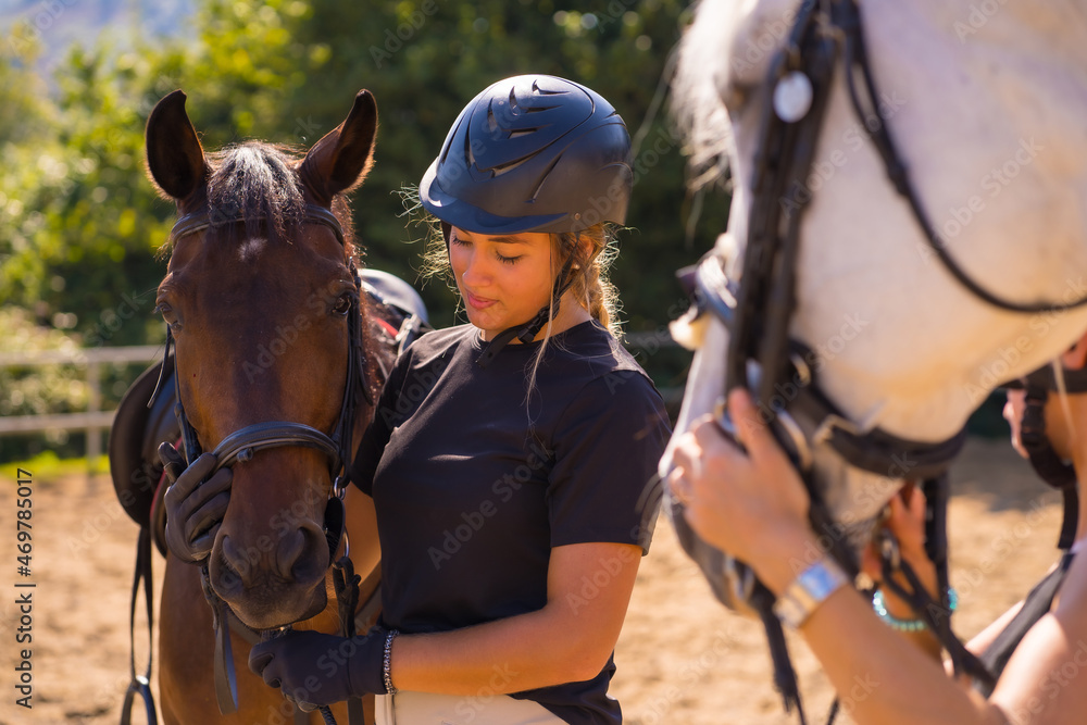 Obraz premium Posing of two young Caucasian girls riders with their white and brown horses on a horse, dressed in black with safety caps