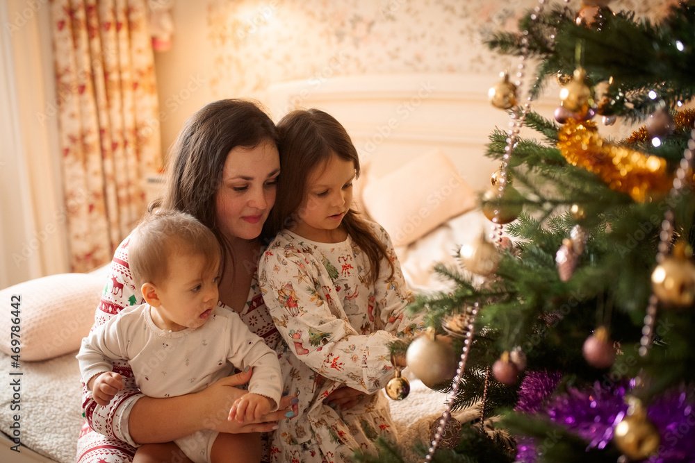 Mom and children sit on the bed at home in front of the Christmas tree and decorate it Mom and children sit on the bed at home in front of the Christmas tree and decorate it