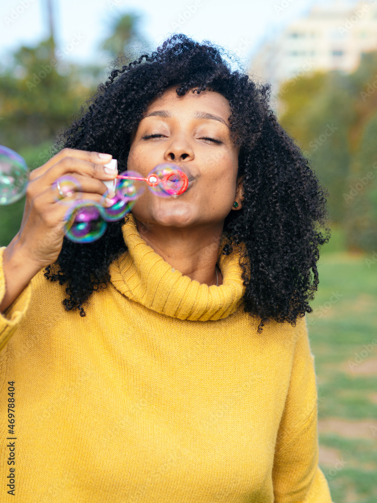 Smiling African American young woman blowing soap bubbles in a park. Happy woman 