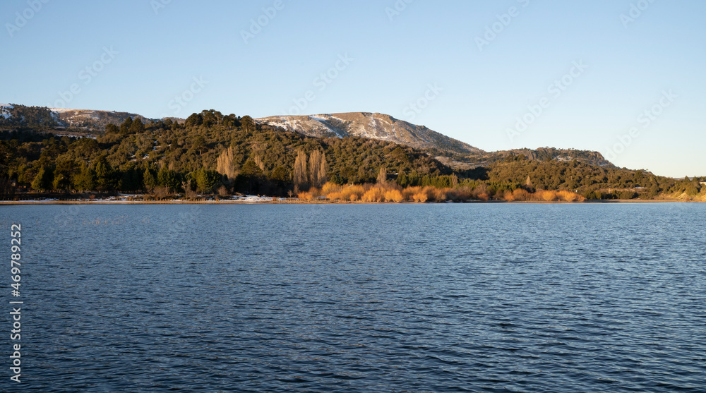 The blue water lake at sunset. The shoreline, forest and mountains in the background. The blue water lake at sunset. The shoreline, forest and mountains in the background.