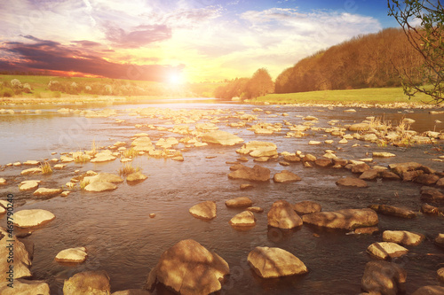Landscape with stones in water rapid of a river against a forest and a sky with a sunset