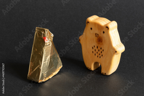 Triangular cream cheeses wrapped in foil next to wooden toy in shape of bear on ablack background. Portioned triangular cheeses. Food for children photo