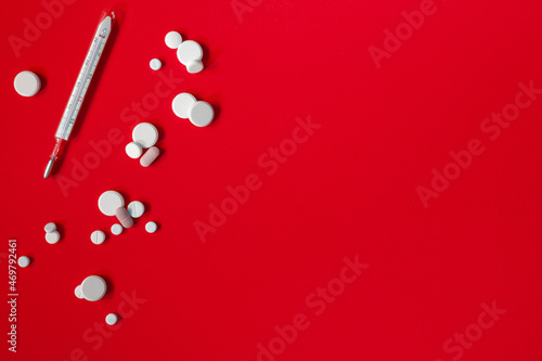 Medical thermometer and a lot of antipyretic pills or antibiotics on red background. Concept of danger and treatment of diseases occurring with high temperature © LariBat