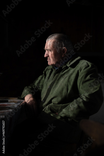 Portrait of the sad grandfather in a green jacket. Natural light interior