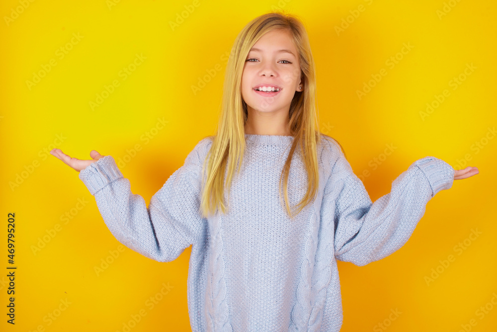 Cheerful cheery optimistic caucasian kid girl wearing blue knitted sweater over yellow background holding two palms copy space Cheerful cheery optimistic caucasian kid girl wearing blue knitted sweater over yellow background holding two palms copy space