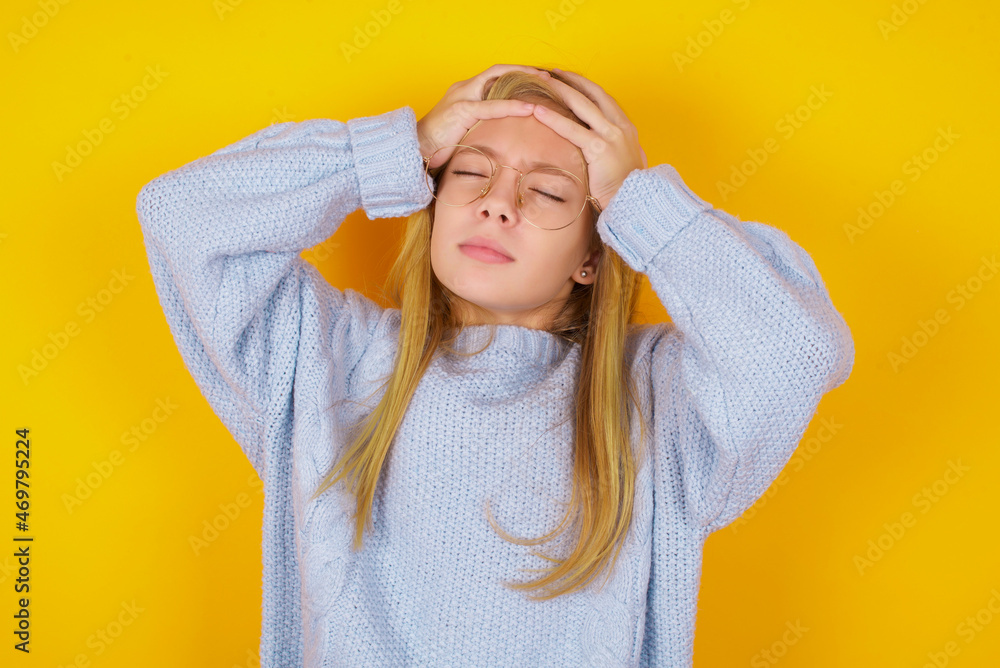 caucasian kid girl wearing blue knitted sweater over yellow background suffering from strong headache desperate and stressed because of overwork. Depression and pain concept. caucasian kid girl wearing blue knitted sweater over yellow background suffering from strong headache desperate and stressed because of overwork. Depression and pain concept.