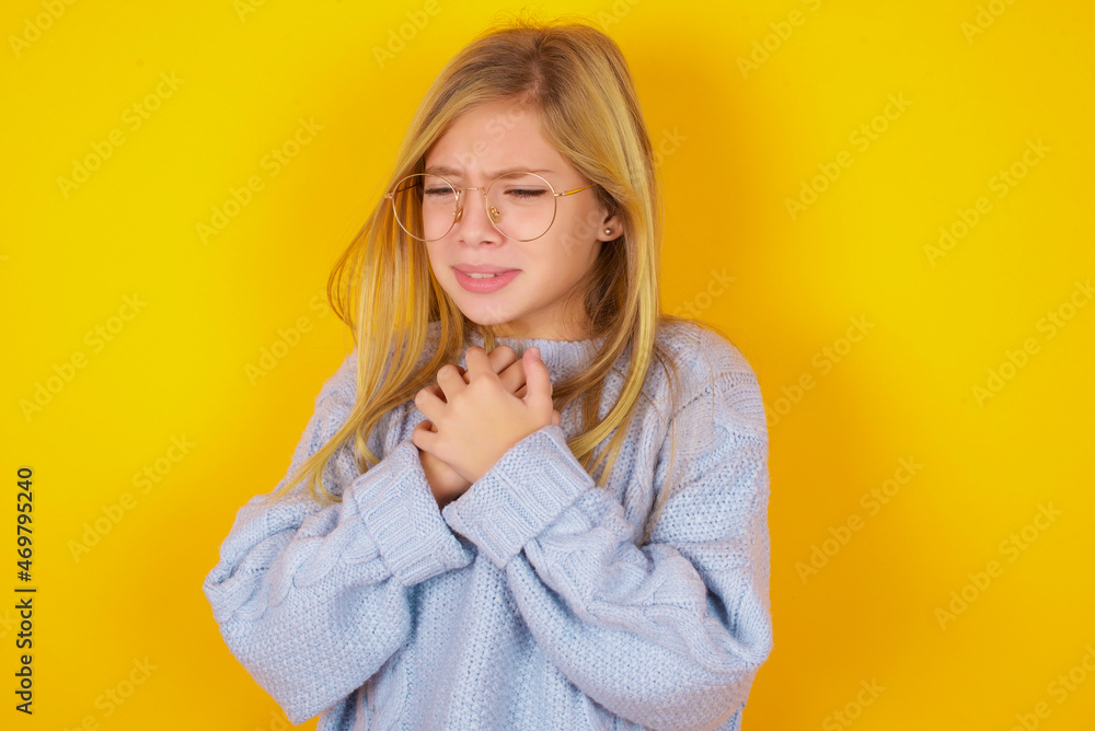 Sad caucasian kid girl wearing blue knitted sweater over yellow background desperate and depressed with tears on her eyes suffering pain and depression in sadness facial expression and emotion Sad caucasian kid girl wearing blue knitted sweater over yellow background desperate and depressed with tears on her eyes suffering pain and depression in sadness facial expression and emotion