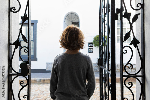 A boy standing looking out of open ironwork gates.  photo