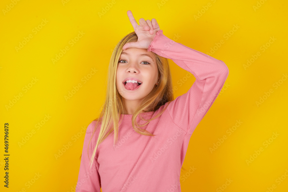 caucasian little kid girl wearing long sleeve shirt over yellow background gestures with finger