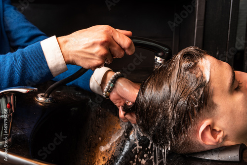 Professional barber washes clients head before haircut at barbershop