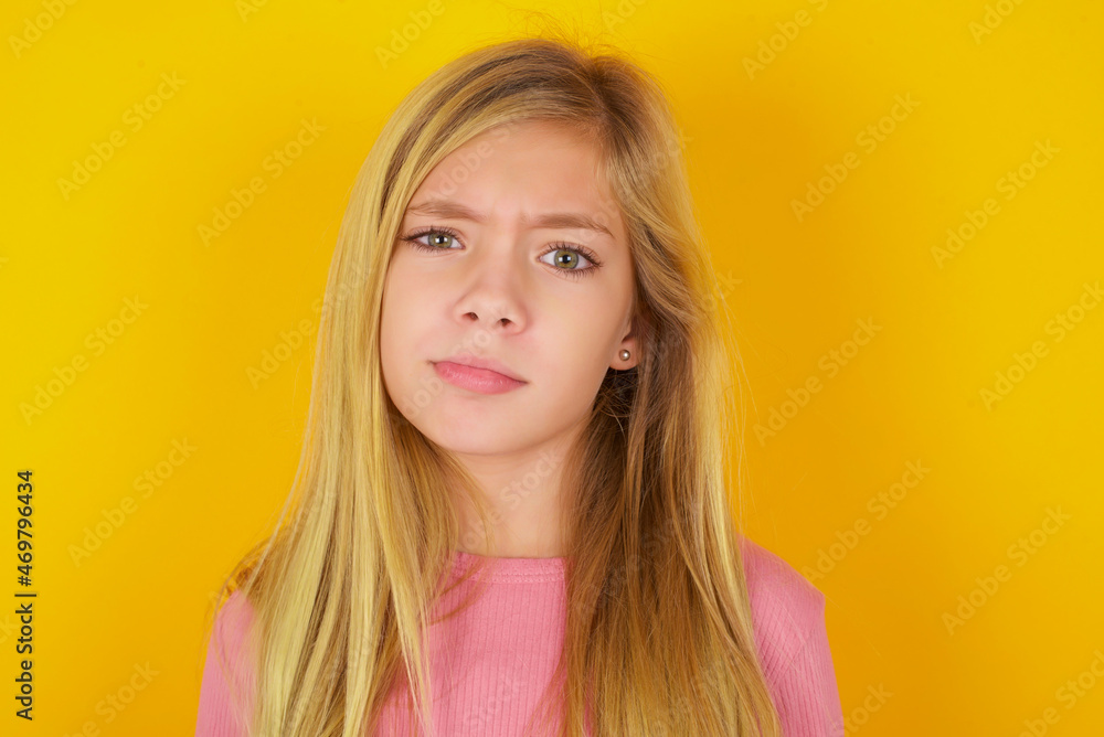 Displeased caucasian little kid girl wearing long sleeve shirt over yellow background frowns