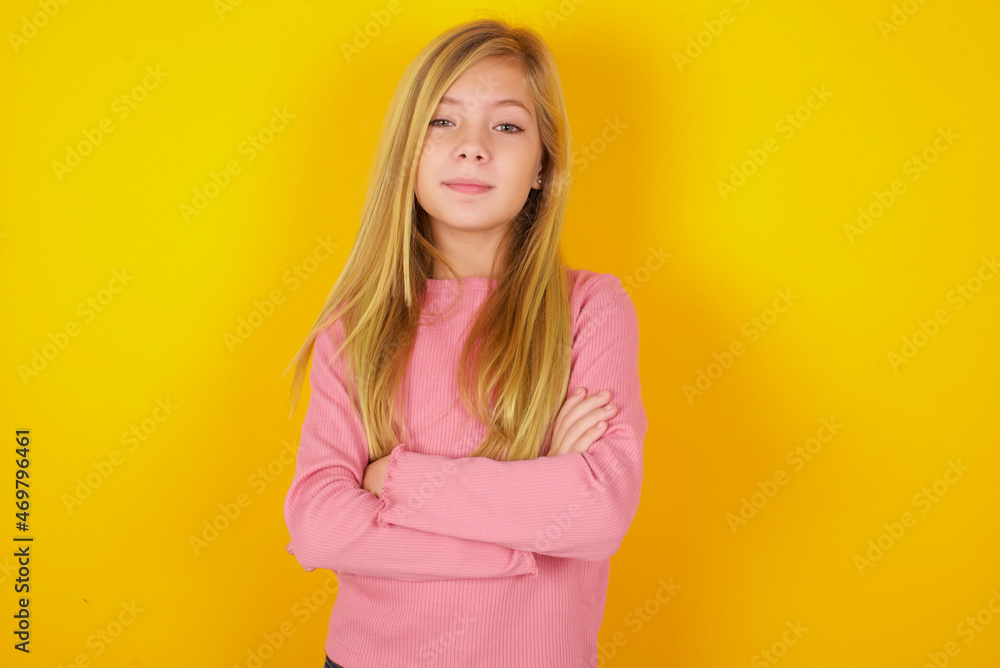 Confident caucasian little kid girl wearing long sleeve shirt over yellow background with arms crossed looking to the camera Confident caucasian little kid girl wearing long sleeve shirt over yellow background with arms crossed looking to the camera