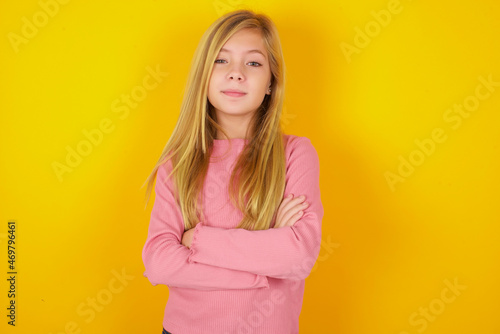 Confident caucasian little kid girl wearing long sleeve shirt over yellow background with arms crossed looking to the camera