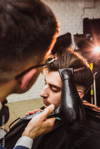 Professional barber dries up clients hair with hair dryer at barbershop poit of view photo from behind photo