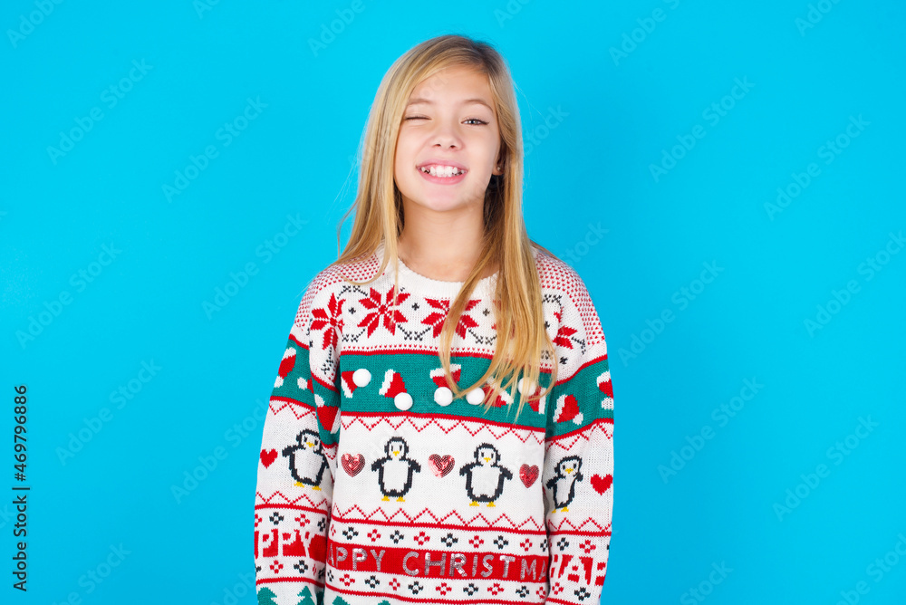 caucasian little kid girl wearing knitted sweater christmas over blue background blinking eyes with pleasure having happy expression. Facial expressions and people emotions concept. caucasian little kid girl wearing knitted sweater christmas over blue background blinking eyes with pleasure having happy expression. Facial expressions and people emotions concept.