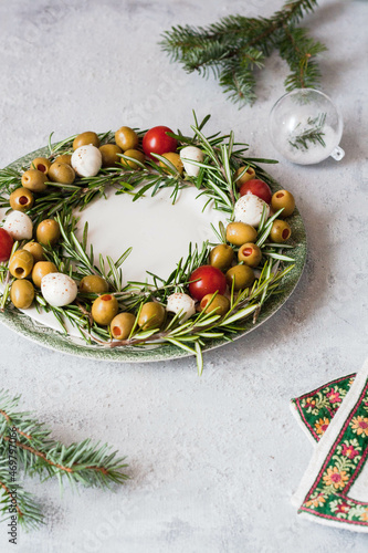 Christmas dish in the form of a wreath of rosemary, olives , mozzarella and cherry tomatoes, Christmas decor with a napkin and a tree toy. 