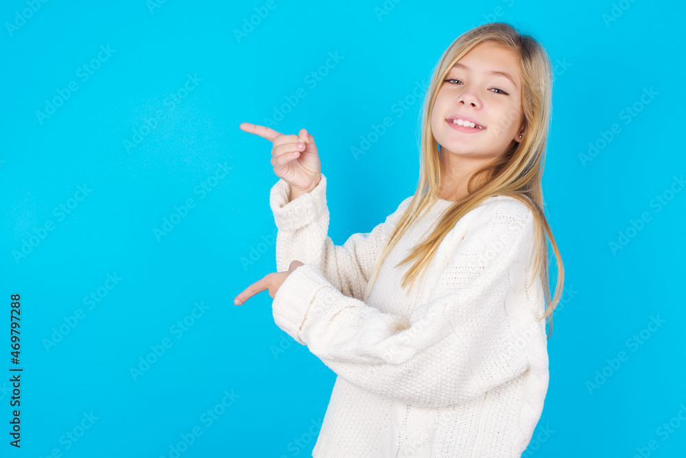 caucasian little kid girl wearing wool jersey over blue background points aside with surprised expression with mouth opened, shows something amazing. Advertisement concept. caucasian little kid girl wearing wool jersey over blue background points aside with surprised expression with mouth opened, shows something amazing. Advertisement concept.