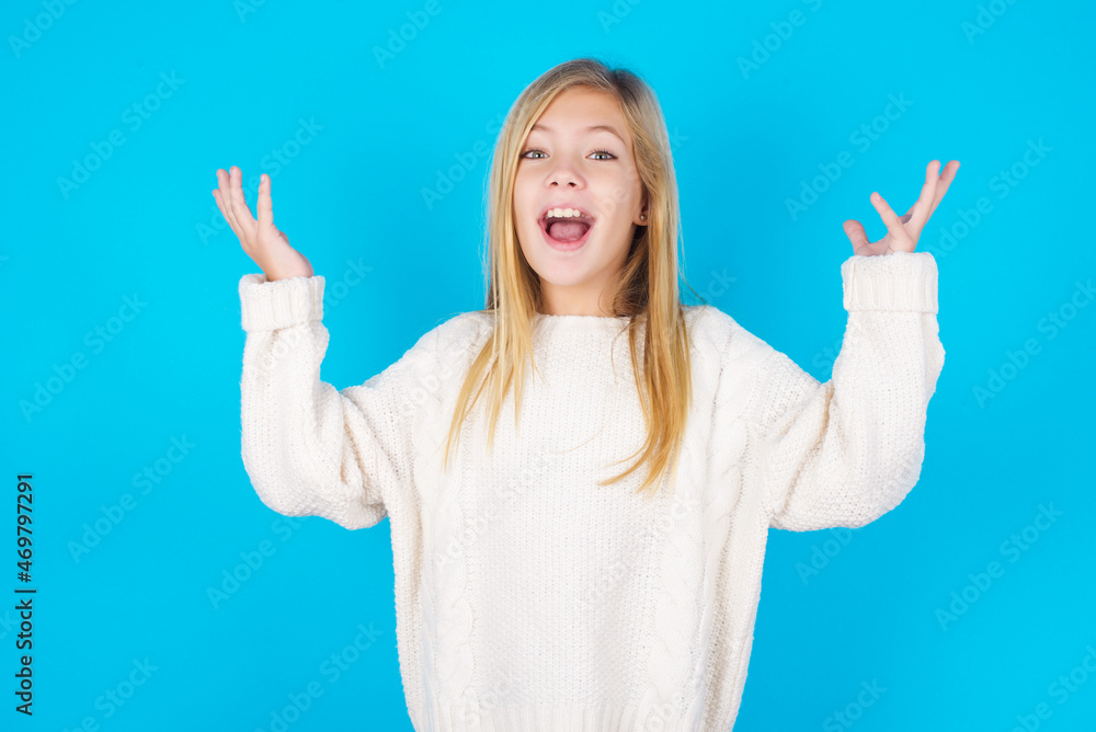 Joyful excited lucky caucasian little kid girl wearing wool jersey over blue background cheering, celebrating success, screaming yes with clenched fists Joyful excited lucky caucasian little kid girl wearing wool jersey over blue background cheering, celebrating success, screaming yes with clenched fists