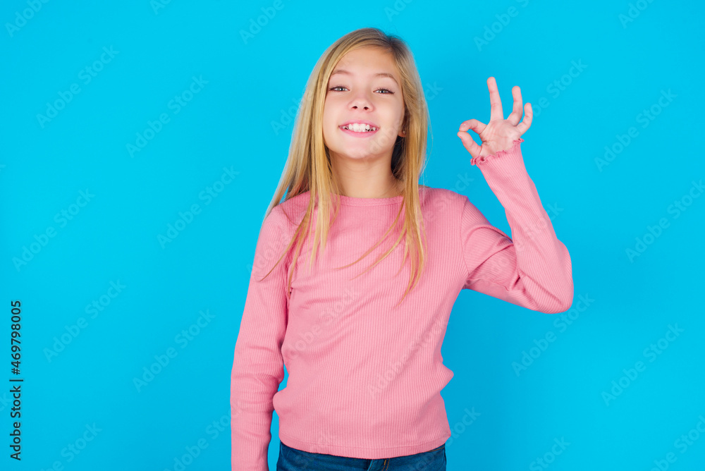 caucasian little kid girl wearing long sleeve shirt over blue background hold hand arm okey symbol toothy approve advising novelty news caucasian little kid girl wearing long sleeve shirt over blue background hold hand arm okey symbol toothy approve advising novelty news