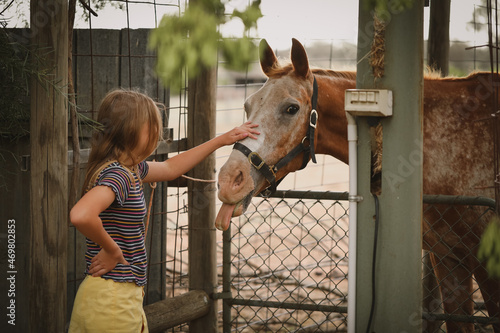 Girl standing at fence patting pet horse with tongue poking out