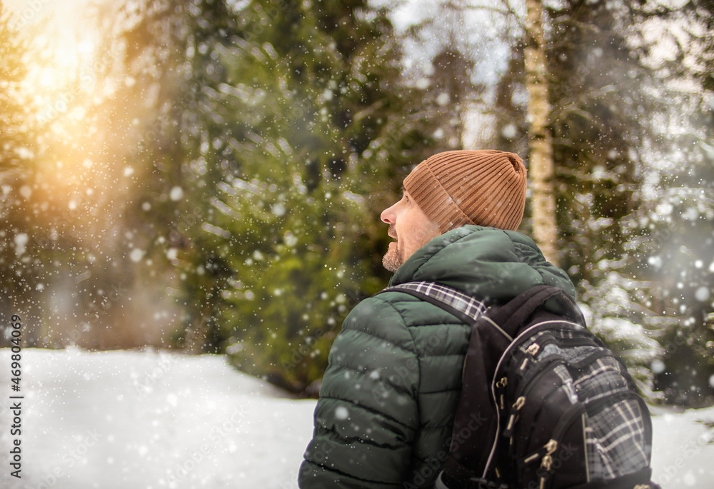 Man with a backpack in the forest enjoys solitude and looks at snowflakes.