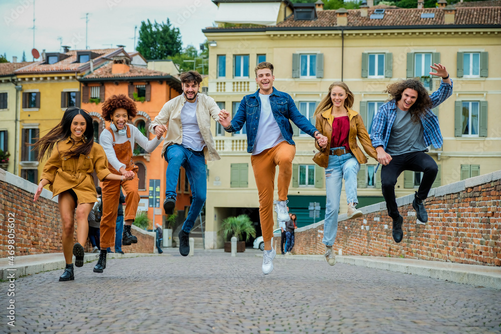 Fototapeta premium Multiethnic group of crazy young people having fun walking and jumping in the city street - Lifestyle and friendship concept