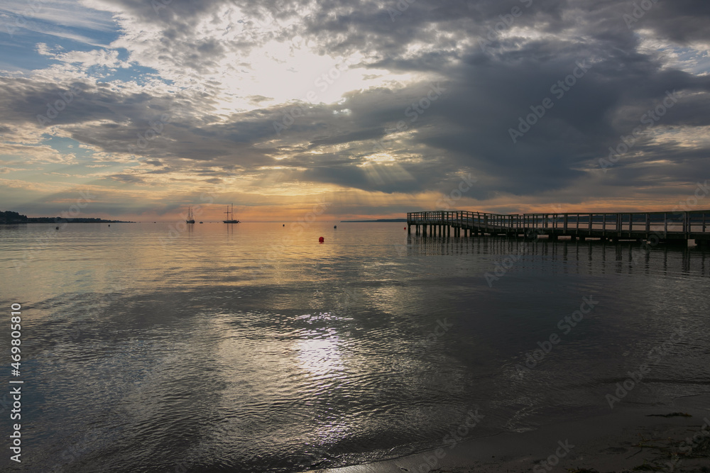 Beach scene with silhouette of pier and sailing vessels in the bay.