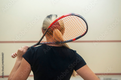 blonde girl stands with her back and holds a racket for squash games