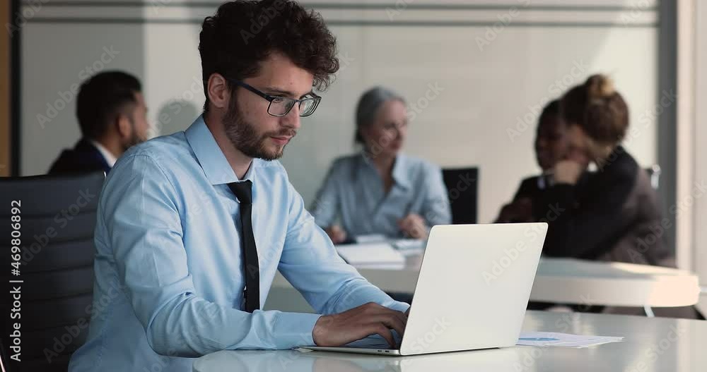 Young entrepreneur man in glasses take notes, do market research use internet and wireless computer working sit at desk in office with diverse businesspeople. Modern tech, e-learn, workflow concept Young entrepreneur man in glasses take notes, do market research use internet and wireless computer working sit at desk in office with diverse businesspeople. Modern tech, e-learn, workflow concept