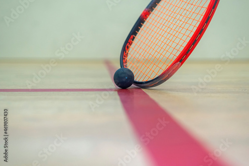 the squash racket and ball lie on the wooden floor between the lines dividing the squash zones