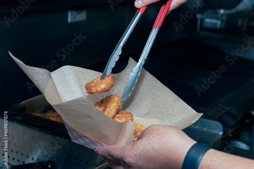 Fresh batch of deep fried calamari rings transfered from deep fryer to cardboard boat with metal tongs photo