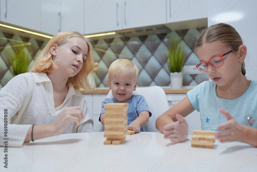 children playing Jenga tower to remove wooden blocks at home. two girls and boy having fun together - board game and kids leisure concept children playing Jenga tower to remove wooden blocks at home. two girls and boy having fun together - board game and kids leisure concept