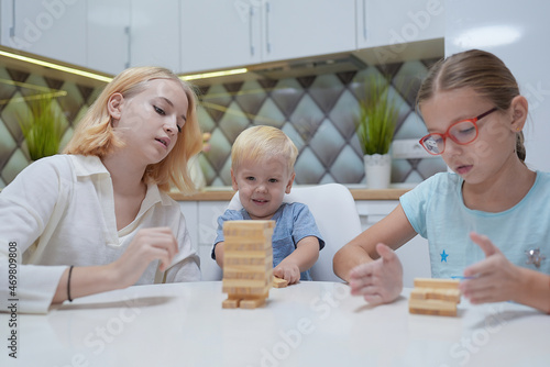children playing Jenga tower to remove wooden blocks at home. two girls and boy having fun together - board game and kids leisure concept