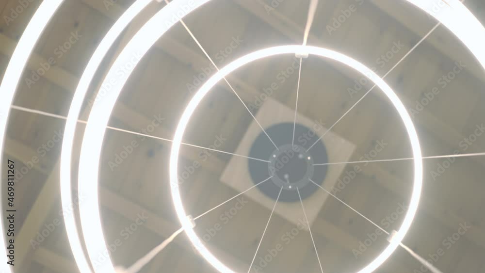Bottom view elegant illuminated chandelier hanging on ceiling indoors. Close-up round circles shining with cold light in home or shop. Live camera spinning in slow motion Bottom view elegant illuminated chandelier hanging on ceiling indoors. Close-up round circles shining with cold light in home or shop. Live camera spinning in slow motion
