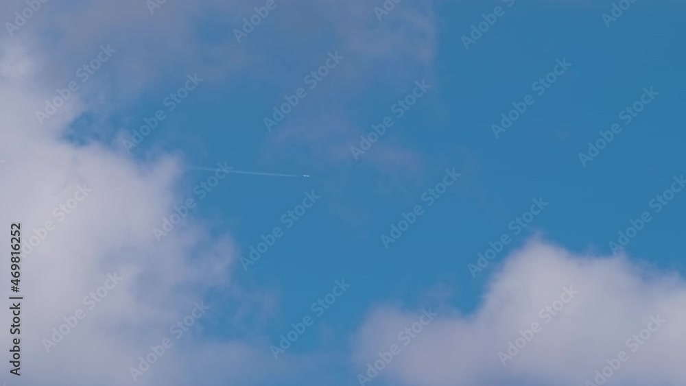 Distant passenger jet plane flying on high altitude on blue sky with white clouds leaving smoke trace of contrail behind. Air traveling concept Distant passenger jet plane flying on high altitude on blue sky with white clouds leaving smoke trace of contrail behind. Air traveling concept