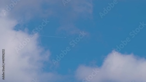 Distant passenger jet plane flying on high altitude on blue sky with white clouds leaving smoke trace of contrail behind. Air traveling concept