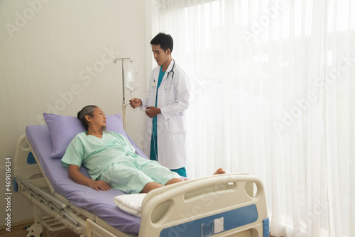 Asian male doctor talking to Asian male patient lying on hospital bed and health services.
