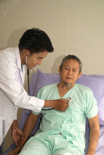 An Asian male doctor examining an elderly Asian male patient using a chest heart rate monitor. 