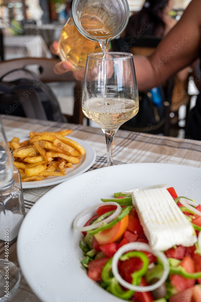 Dinner with white wine in Greek taverna, vegetable greek salad, fried potatoes