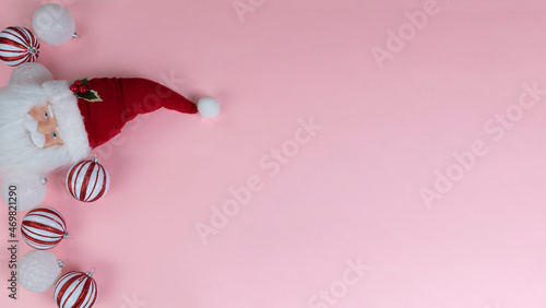 Christmas holiday ball ornaments plus Santa Claus decoration on light pink background in overhead view