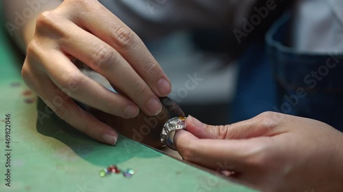 Close-up gems on table in workshop with female hands engraving stones in silver ring in slow motion. Unrecognizable expert skilled Caucasian woman working in jewellery workshop indoors photo