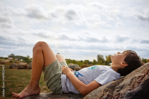 A young boy lays back on rock barefoot in sunshine