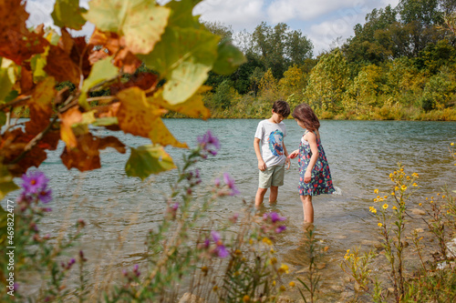 A little boy and girl stand together wading in a lake in summer