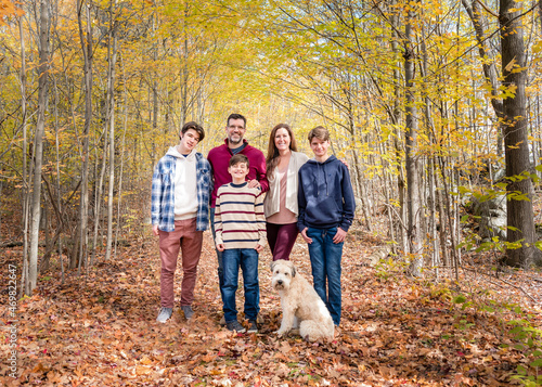 Portrait of family of five outside in wooded area on autumn day.