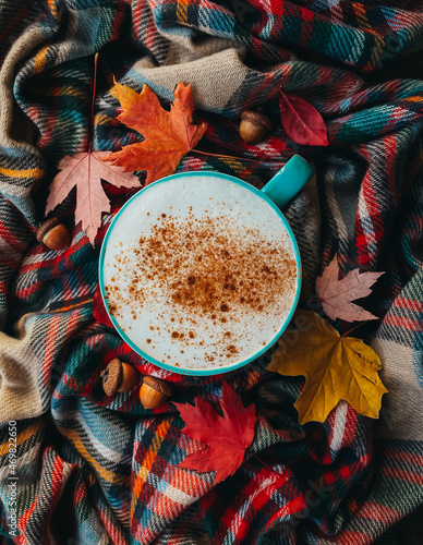 Overhead of pumpkin spice latte on plaid fall scarf with leaves photo