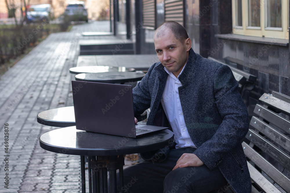 Young man sitting at a table in a cafe with his laptop outside. He looks at the camera Young man sitting at a table in a cafe with his laptop outside. He looks at the camera