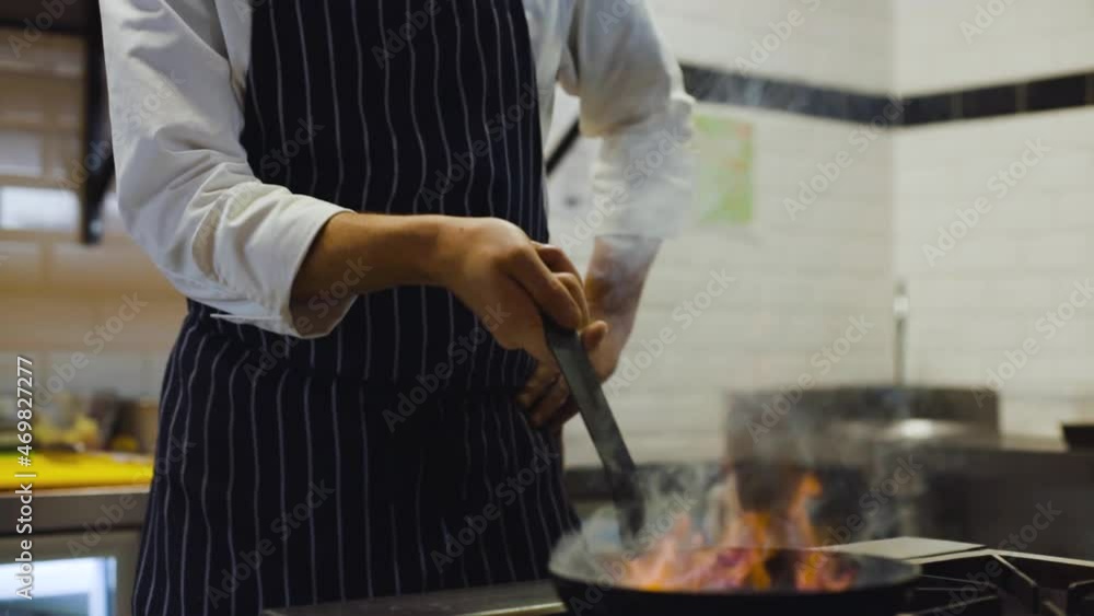 Slow motion of chef cooking with fire provokes flames in pan in a professional kitchen Slow motion of chef cooking with fire provokes flames in pan in a professional kitchen